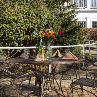 A sunny outdoor patio with a table set for dining, adorned with a vase of colorful flowers.