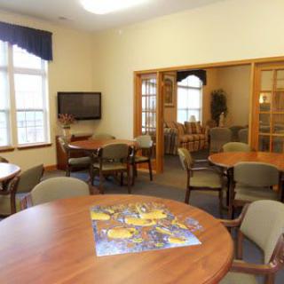 A cozy meeting room with tables, chairs, and a television, featuring a partially completed puzzle on one of the tables.