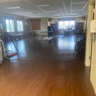 A spacious exercise room featuring wooden flooring and large windows, equipped with various exercise machines.
