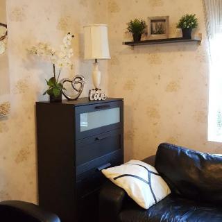 A cozy living room with a black couch, decorative shelf, and lamp.