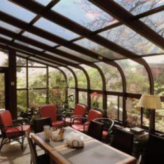 A cozy conservatory with glass walls and ceiling, filled with natural light and surrounded by lush greenery.