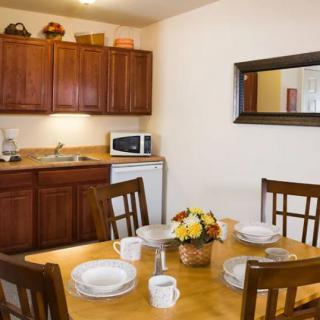 A cozy dining area with a wooden table set for four, adjacent to a kitchen with cabinets and appliances.
