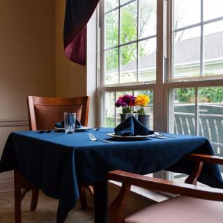 A cozy dining setup by the window, featuring a blue tablecloth and a bouquet of flowers.