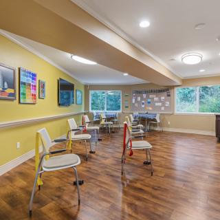 A spacious community room with chairs arranged in a circle, featuring hardwood floors and colorful artwork on the walls.