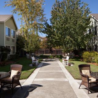 A serene garden pathway lined with tables and chairs between two residential buildings.