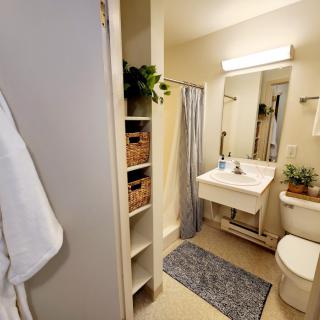 A well-organized bathroom with a sink, toilet, and shower area, complemented by shelves and a bath mat.