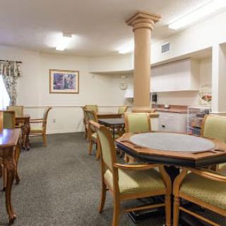 A cozy dining and kitchen area with several tables and chairs, featuring soft lighting and classical decor.