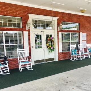 A welcoming entrance with rocking chairs and a decorative wreath on a brick building.
