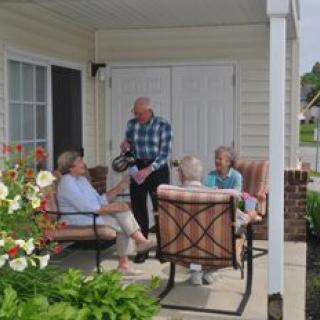 A group of seniors sitting and conversing on a porch surrounded by garden plants.