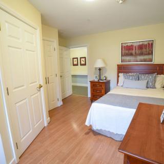 A cozy bedroom with a neatly made bed, wooden dresser, and warm lighting.