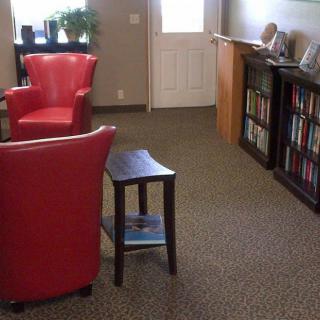 A cozy living space featuring red chairs, bookshelves filled with books, and potted plants.