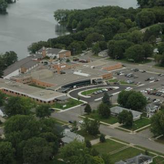 An aerial view of a commercial complex near a lake, surrounded by greenery.