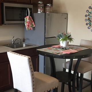 A cozy kitchen and dining area with a table and chairs, featuring a refrigerator, microwave, and decorative elements.