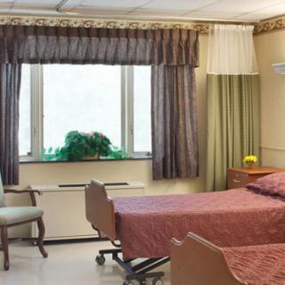 A hospital room with a single bed, chair, and a window with curtains.