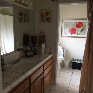 A cozy bathroom with a tiled countertop, mirror, and floral artwork.