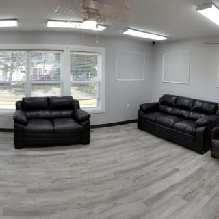 A modern living room with black leather sofas and large windows.