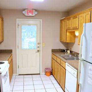 A compact kitchen with wooden cabinets, white appliances, and an exit door.