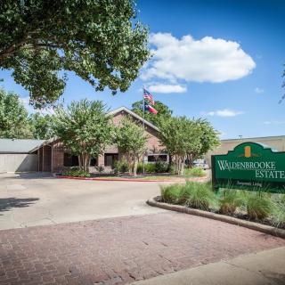 A serene view of a building with a welcoming sign, surrounded by trees and a clear blue sky.