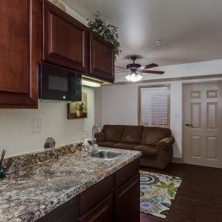 A cozy living space featuring a kitchen area with granite countertops, wooden cabinets, and a comfortable couch in an adjacent living room.