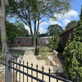 A serene outdoor view showcasing a landscaped area with trees and pathways, framed by a decorative fence.