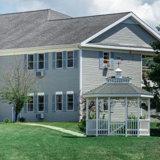A two-story house with a well-kept lawn and a white gazebo in the front yard.