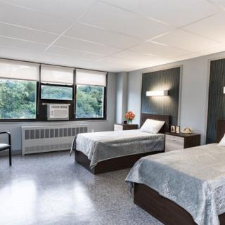 A modern bedroom with two neatly made beds, large windows, and natural light.
