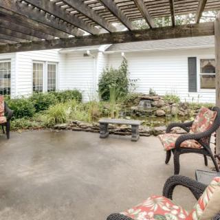 A cozy outdoor patio with seating under a pergola, surrounded by greenery.