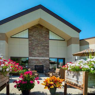 A modern building with a gabled roof surrounded by vibrant flower arrangements on a sunny day.