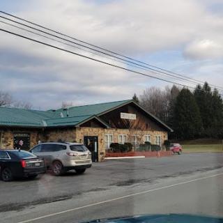 A roadside restaurant with a parking lot and several parked cars on a cloudy day.