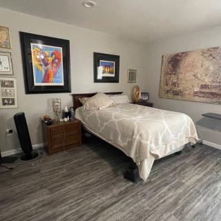 A modern bedroom featuring artwork on the walls, a neatly made bed, and sleek laminate flooring.