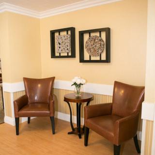 A cozy waiting area with two leather chairs, a small side table with flowers, and framed artwork on the wall.