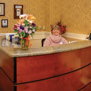 A welcoming receptionist sits at a desk adorned with flowers in an office setting.