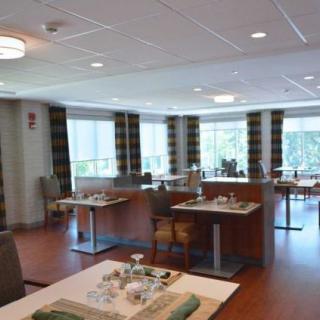 A spacious dining area with neatly arranged tables and chairs, surrounded by large windows with curtains.