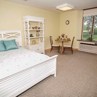 A cozy bedroom with a bed, shelves, and a small dining table by the window.