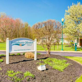 A scenic park entrance with a welcoming sign and blossoming trees under a clear blue sky.