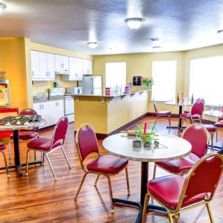 A bright and inviting dining area with red chairs and white tables, adjacent to a kitchen space.