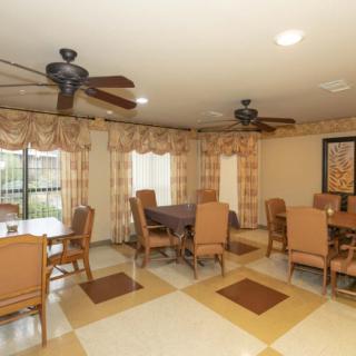 A well-lit dining room featuring multiple tables and chairs, ceiling fans, and decorative curtains.