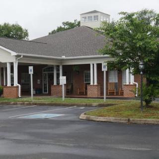 A small brick building with a covered entrance and an adjacent parking lot under an overcast sky.