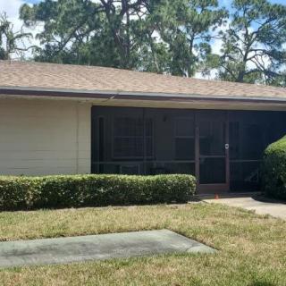 A small house with a screened porch surrounded by trees and shrubs.