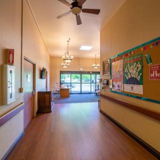 A brightly lit hallway with wooden flooring and a bulletin board on the wall.