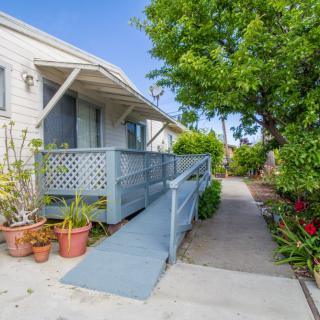 A house with a wooden ramp leading to the entrance surrounded by a garden and potted plants.
