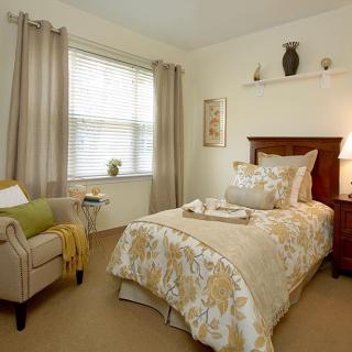 A cozy and elegantly decorated bedroom with a single bed, armchair, and large window.