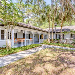 A charming house with a porch surrounded by trees and a garden walkway.