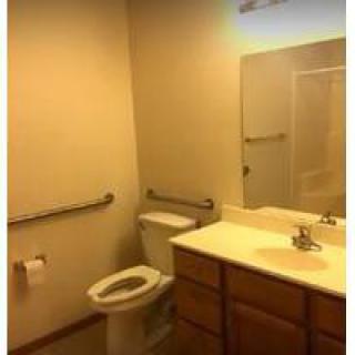 A bathroom interior with a toilet, sink, and mirror, featuring accessibility grab bars.