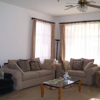 A cozy living room with two sofas and a coffee table, adorned with curtains and a ceiling fan.