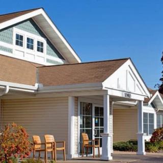 A residential building with a covered front porch and outdoor chairs, set against a clear blue sky.