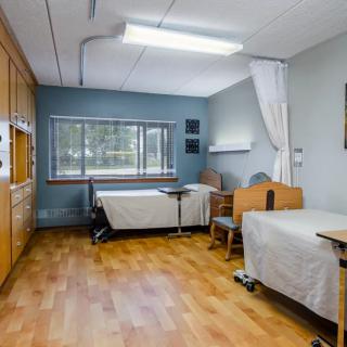 A clean and spacious hospital room with two beds, wooden flooring, and a window providing natural light.
