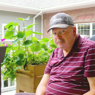 A man sitting on a porch with plants in the background.