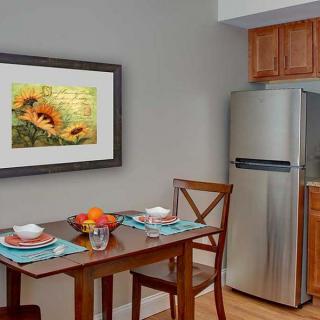 A cozy kitchen nook with a dining table set for two, featuring a sunflower painting and a modern fridge.