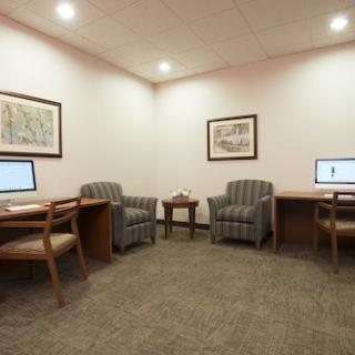 A small office space with two desks, each equipped with a computer, and two upholstered chairs in the center.
